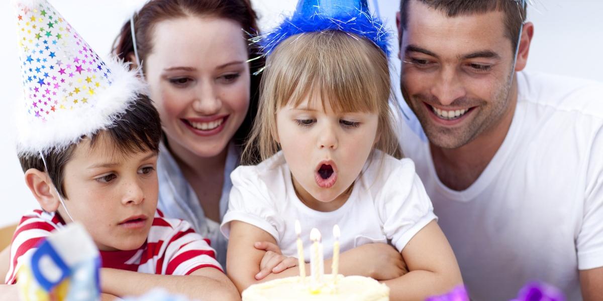 small girl blowing out birthday candles with brother and parents